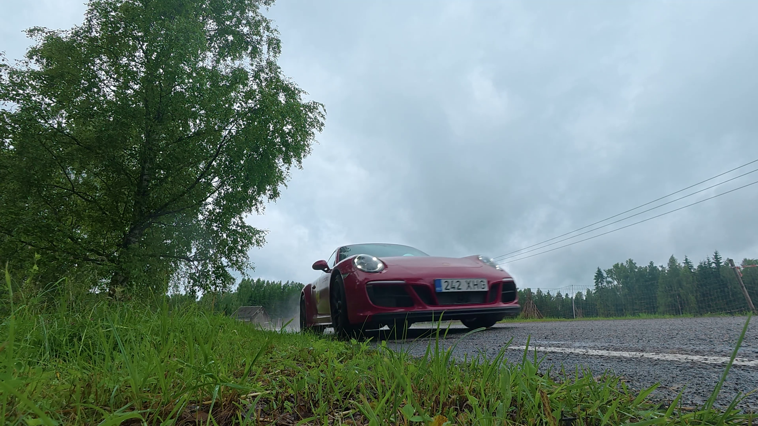 Punane Porsche möödub teeäärsest kaamerast märjal asfaltteel.